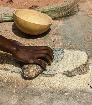 Een Afrikaanse vrouw vermaalt gierst tot meel met traditonele maalstenen in Burkina Faso.