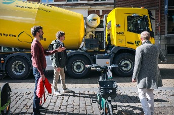 De onderzoekers staan bij een cementwagen in een smalle straat