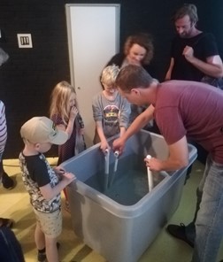 children and adults are holding seal whisker sensors in a tank with water to see how they work