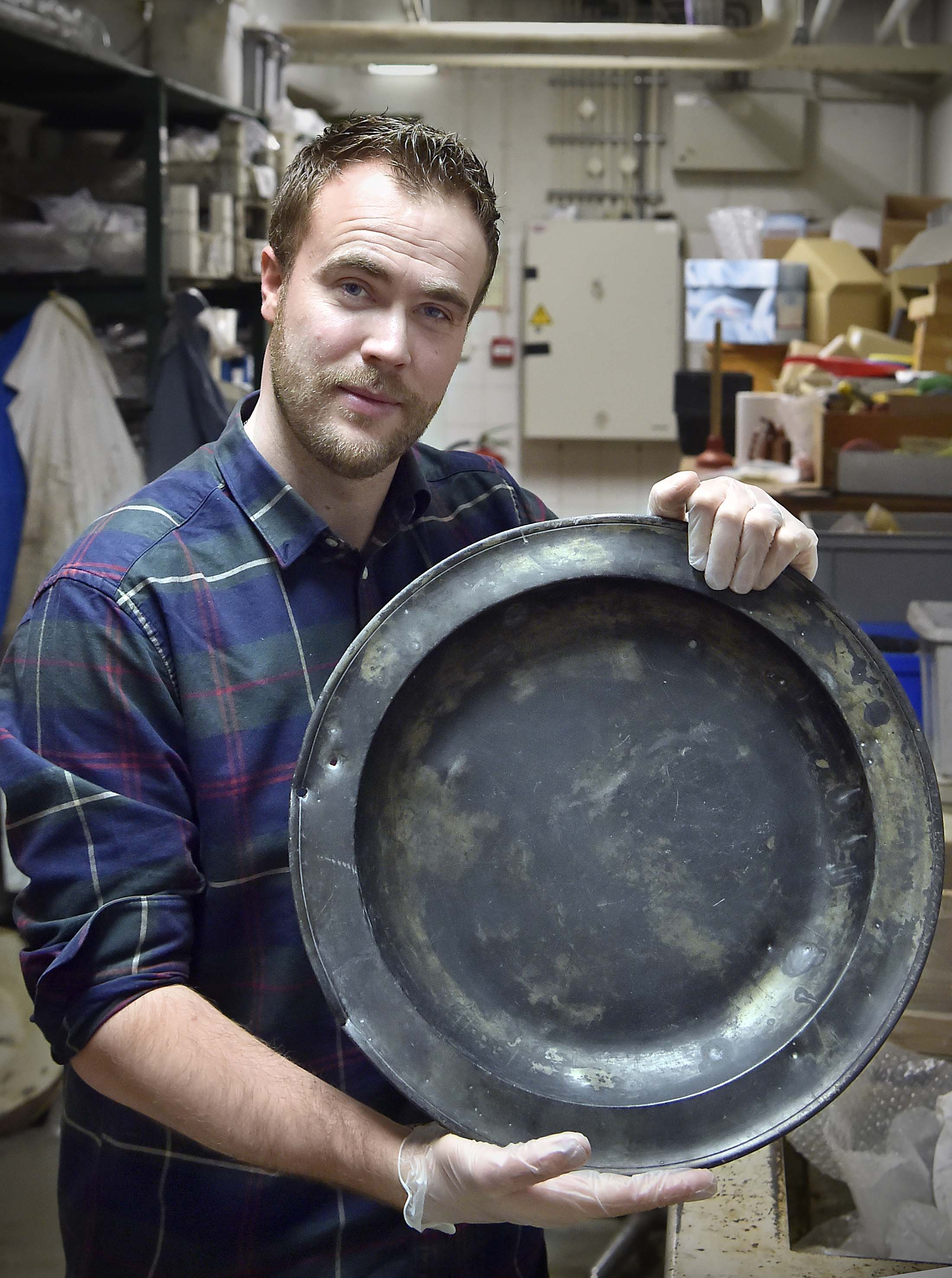 Een tinnen schaal uit Londen, te zien aan de stempels op de achterzijde. De krassporen duiden op gebruik voor eten, maar een spijkergat suggereert dat hij ook aan de wand heeft gehangen, wellicht als versiering.The pewter bowl is from London, as we can tell by the imprints on its back. Scratches indicate that it was used to serve food, but a hole for a nail suggests that it was hung on a wall at some point, perhaps as a decoration.