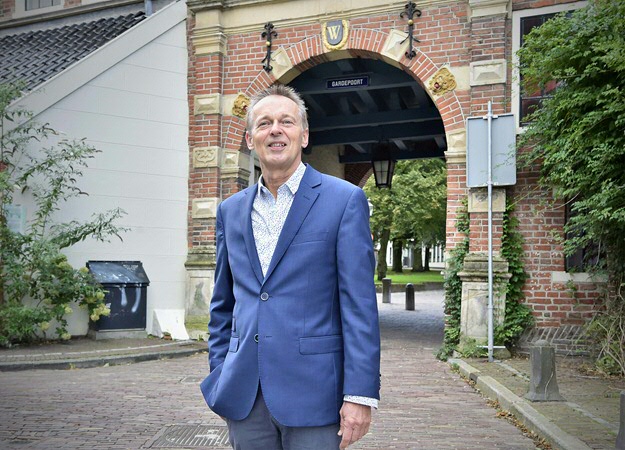 Joop Koopmans, wearing a blue suit-jacket, stands in front of the Gardepoort, a brick gate at the Martinikerkhof in Groningen.