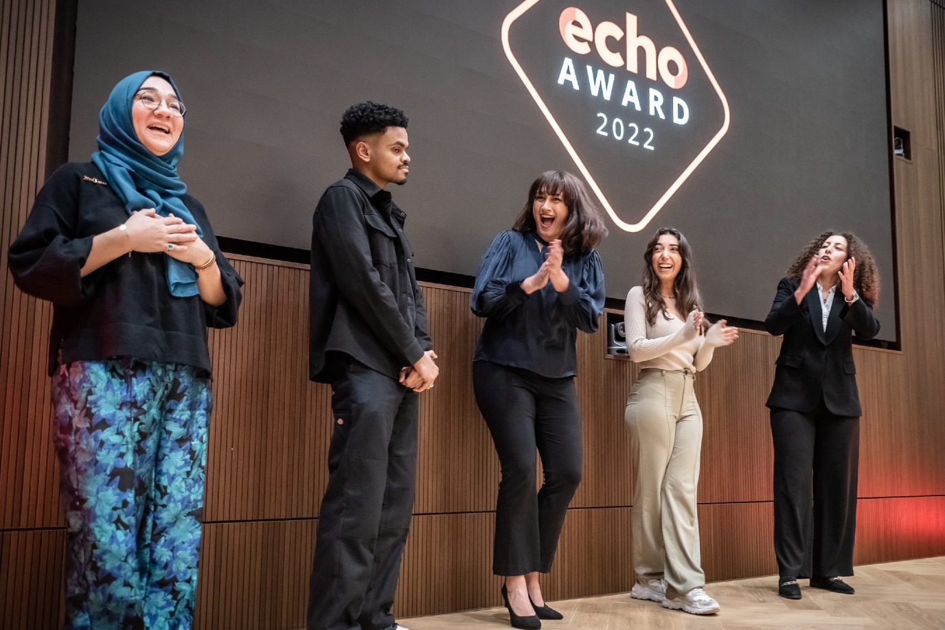 Vijf studenten vieren voor een scherm met de tekst "ECHO Award 2022".