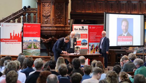 De minister signeert de poster van de lezing. Naast hem Gert de Roo en Johan Woltjer