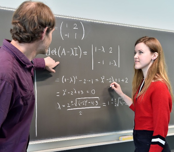 Student and teacher with Mathematics equations on blackboard