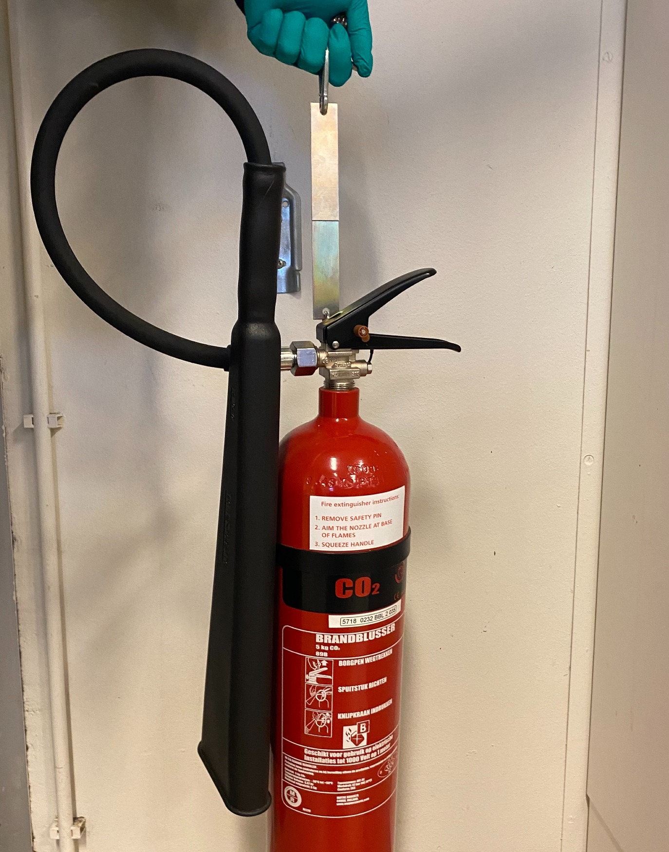 Deze brandblusser en het gewicht hangen aan metalen strips die met lijm aan elkaar zijn geplakt.