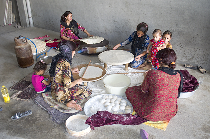 Baking a large amount of bread on a plate oven heated with butane gas. Three women each have their own task in shaping the dough into wafer-thin flaps. A fourth woman bakes the loaves on the oven. Children are present so that knowledge is transferred in a playful way. The objects are made of wood and metal (Boskin, Iraq - June 2014).