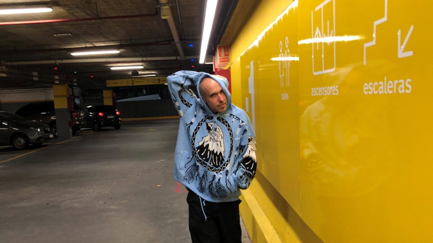 Juan Chao photographed next to the bright yellow wall of a parking garage.