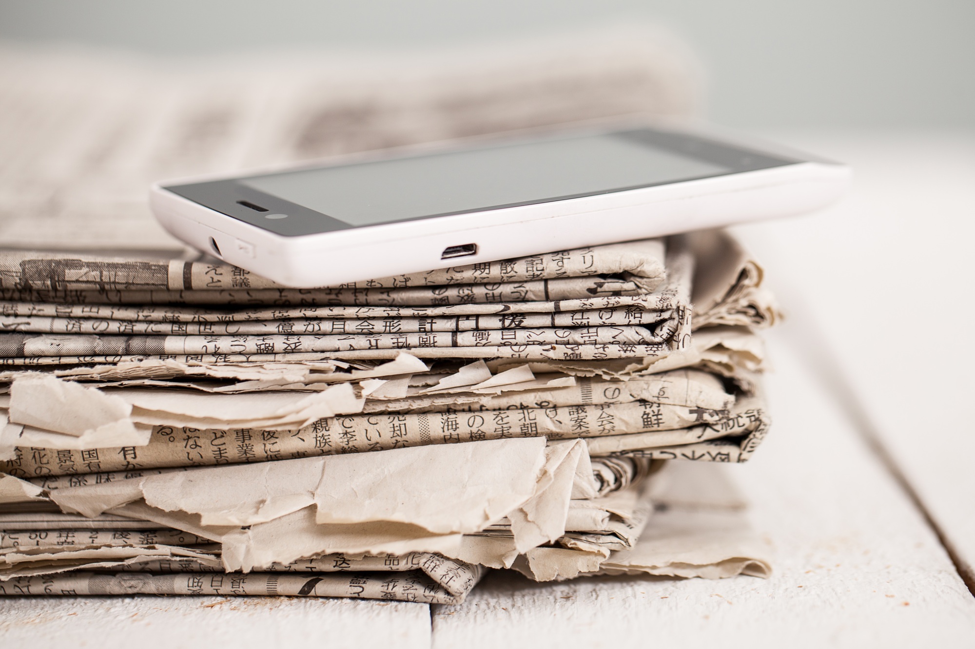 Stack of newspapers with a smartphone on top.