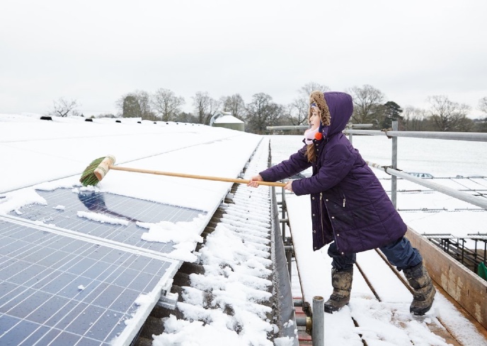 A young girl removes snow from a solar panel.